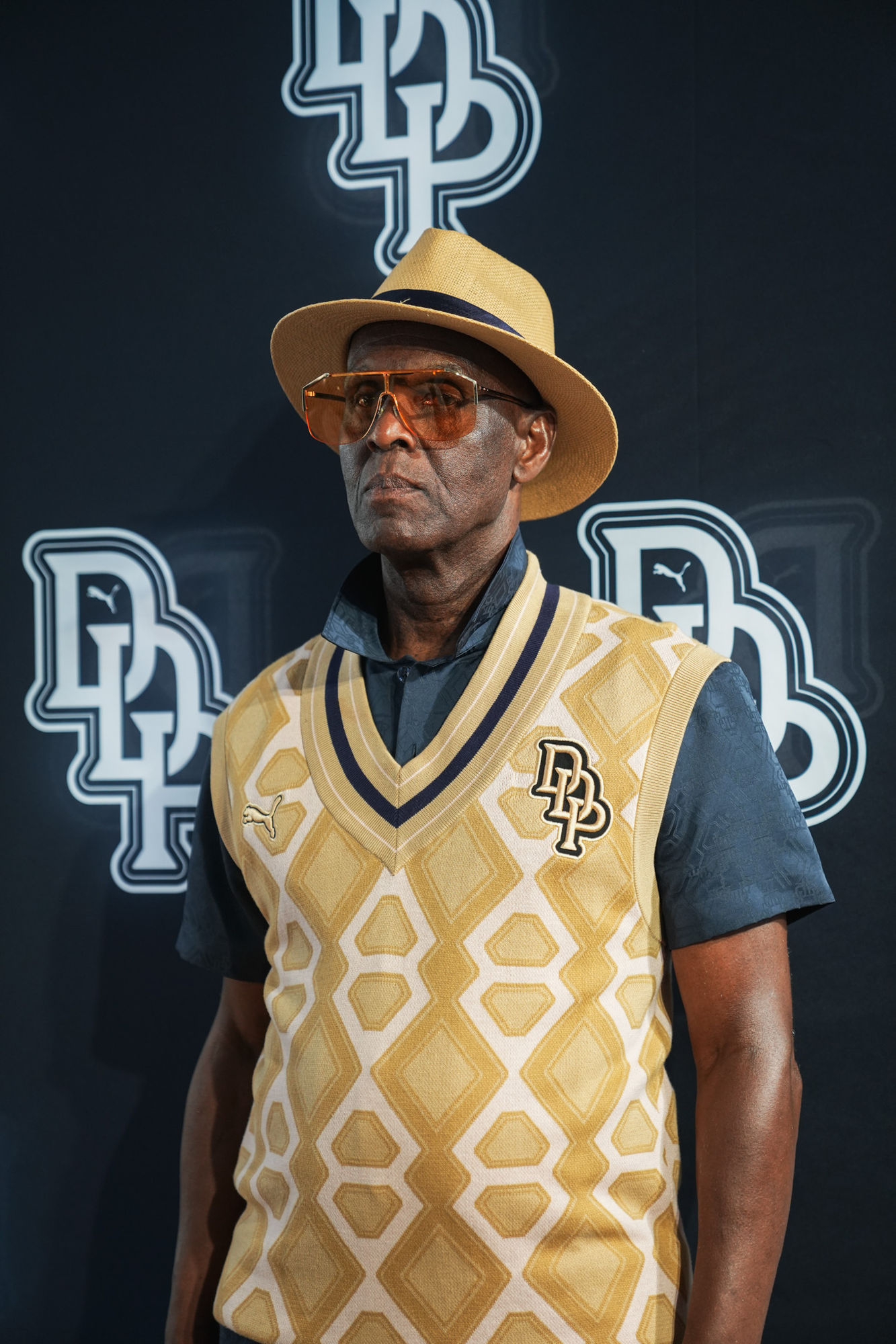 Dapper Dan portrait in the PUMA × Dapper Dan capsule, in front of a branded step-and-repeat